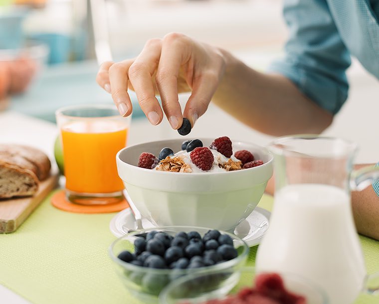 A hand placing a blueberry on top of a fruit and yogurt parfait bowl