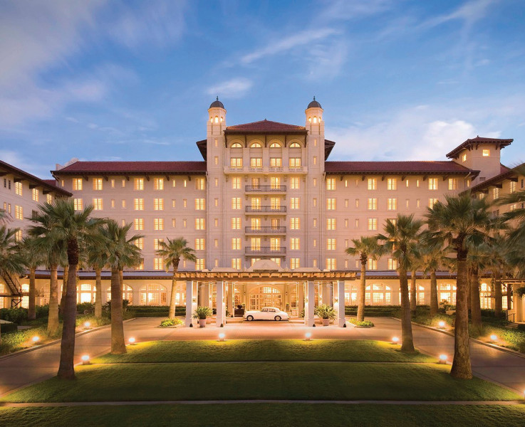 Exterior view of Hotel Galvez lit up at night with a large lawn area lined with palm trees