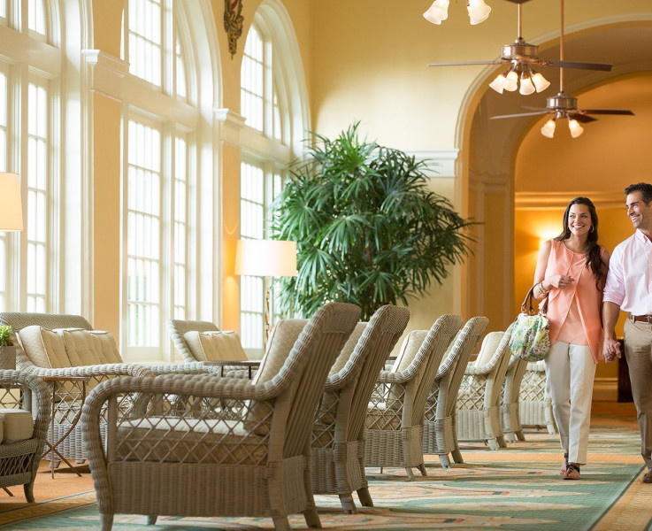 A couple walking down a hallway next to a seating against large windows