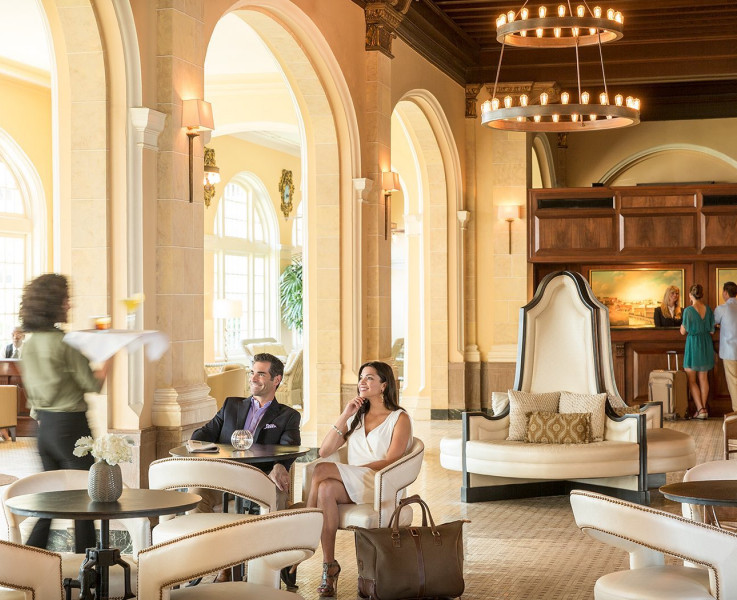 A waitress carrying a tray of drinks walking to a couple seated at the lounge area