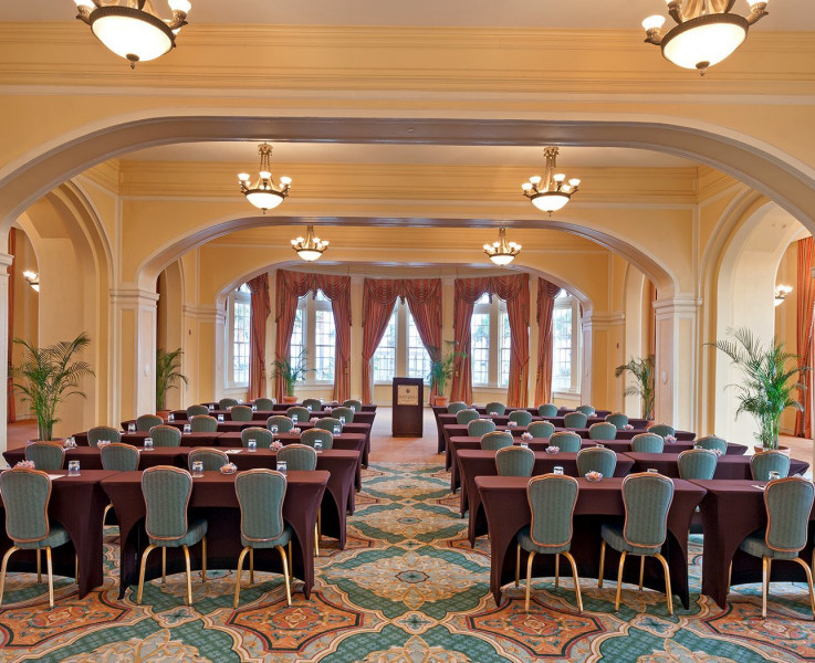 A room set up for an auditorium style meeting with rows of tables and chairs and a podium at the front