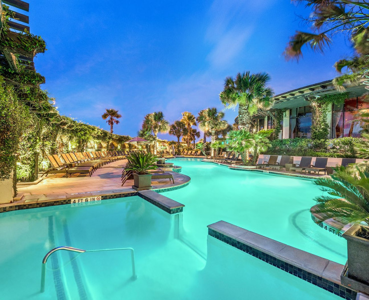 Outdoor pool illuminated at night surrounded by greenery and lounge chairs