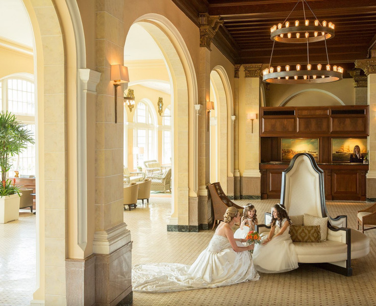 A bride kneeling to be eye level with her two flower girls sitting on a circular couch  