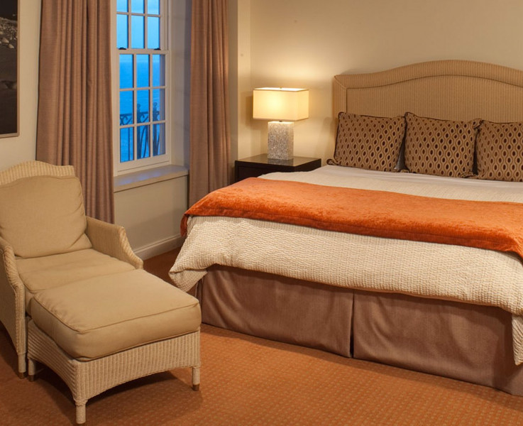 Interior of a room with a king size bed, nightstand, lamp, chair and ottoman
