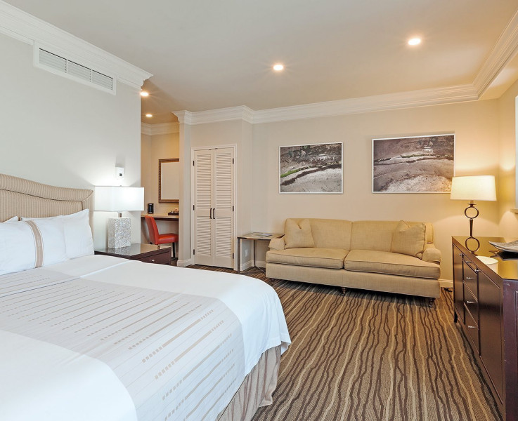 Interior of a room with a king bed, nightstand, dresser, mounted TV, couch, closet, and desk area in distance
